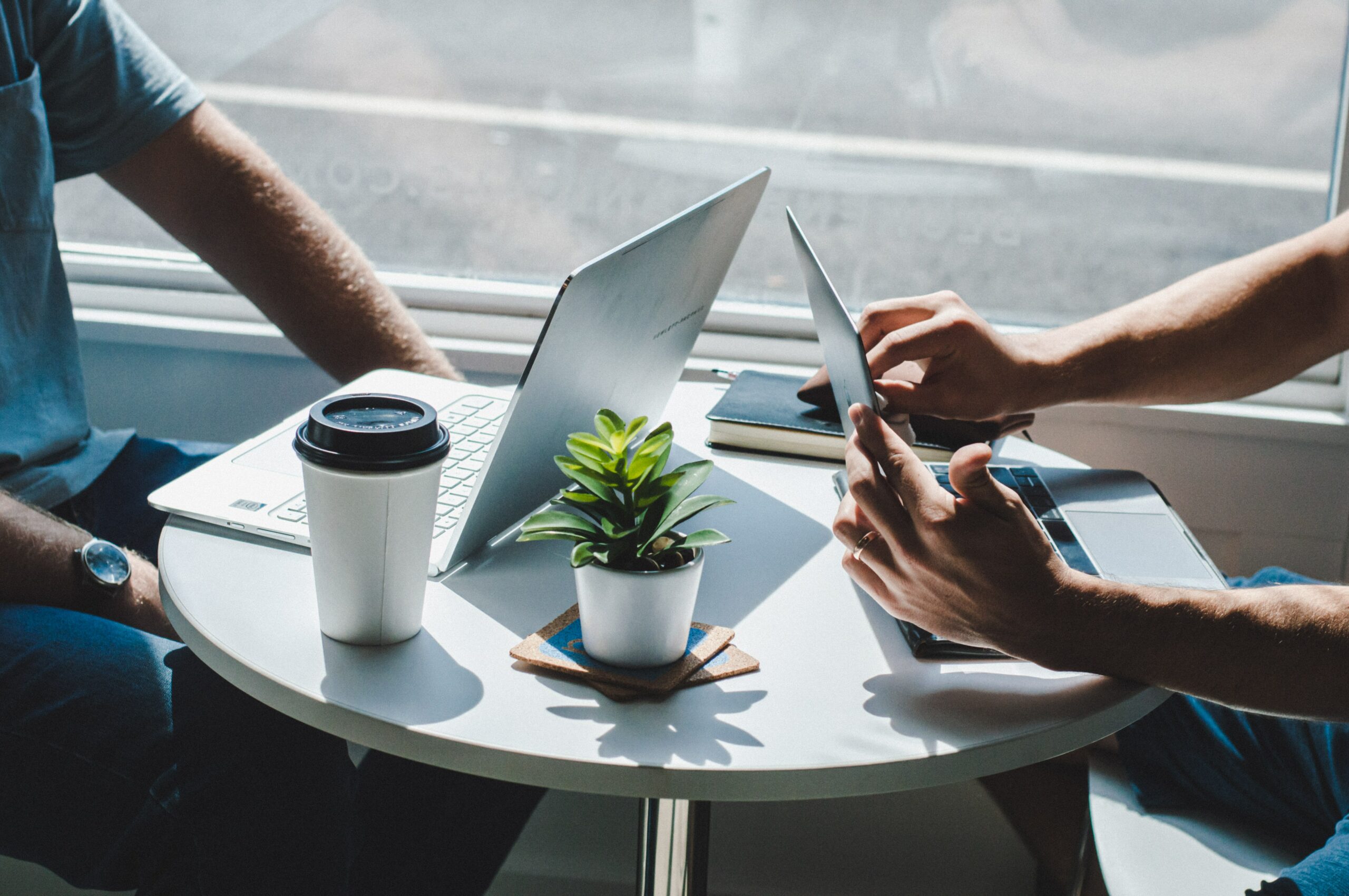 two people sitting at table with laptops and coffee casual meeting interview