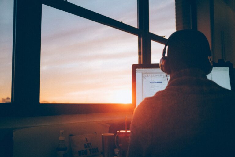 employee with headphones working at computer near window during sunset