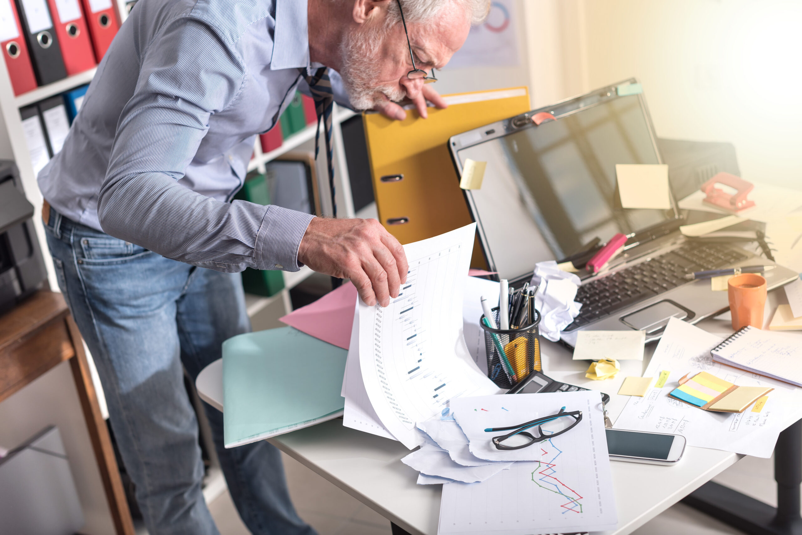 disorganized scheduling reporting paperwork with confused man at desk