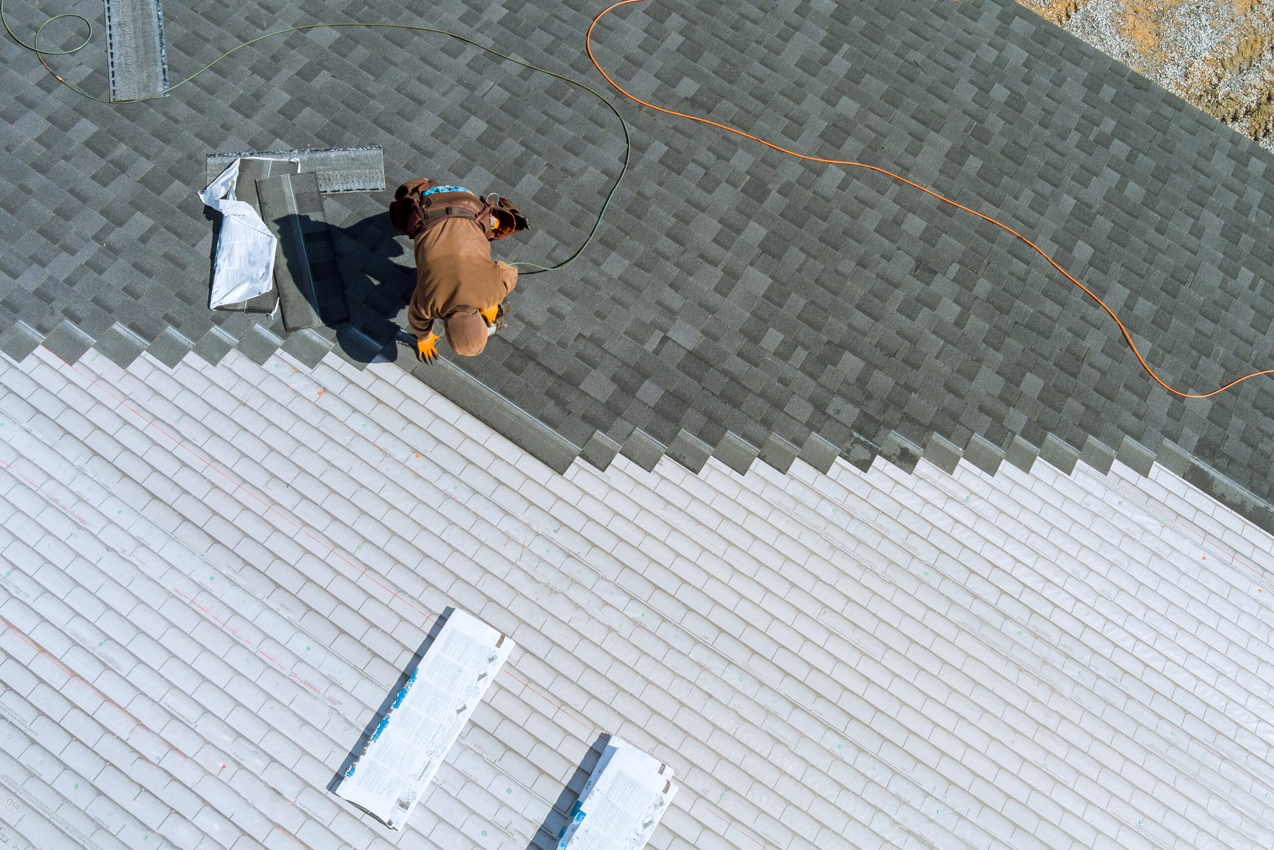 A worker installing shingles on the roof of a home